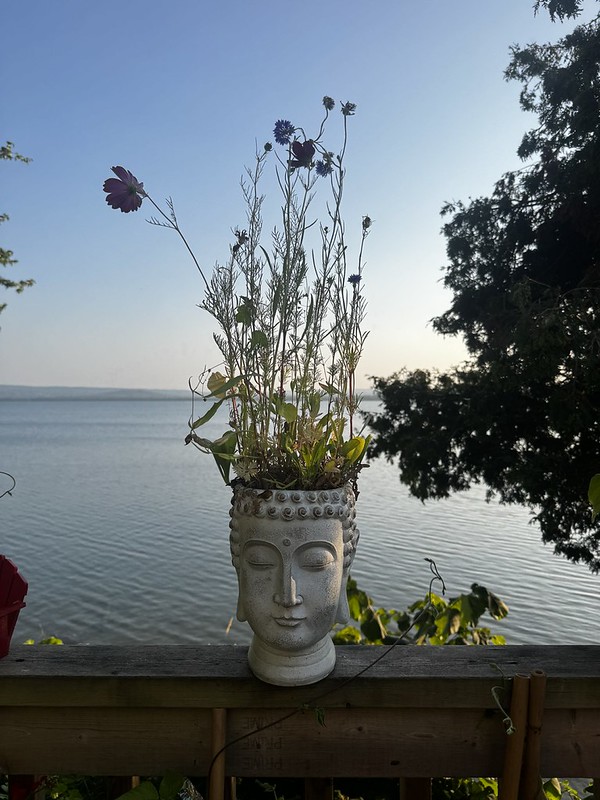 Stone Buddha-head planter holding wildflowers on a wooden railing above Bass Lake at dusk