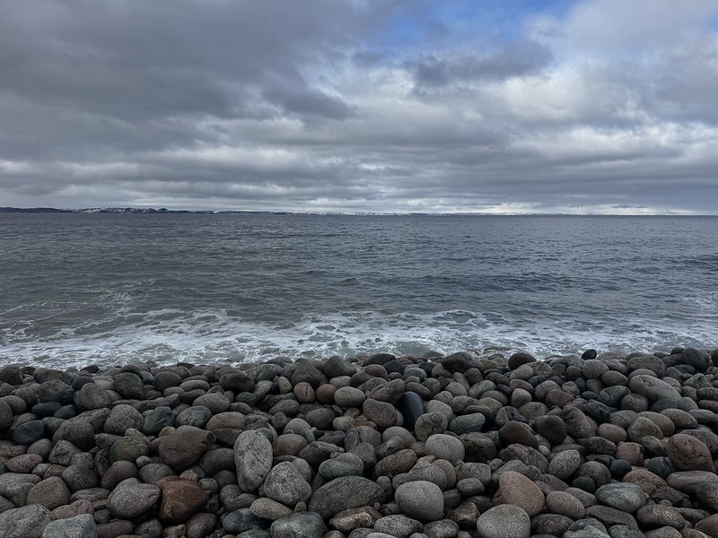 Rocky shoreline meeting cold water under a heavy sky